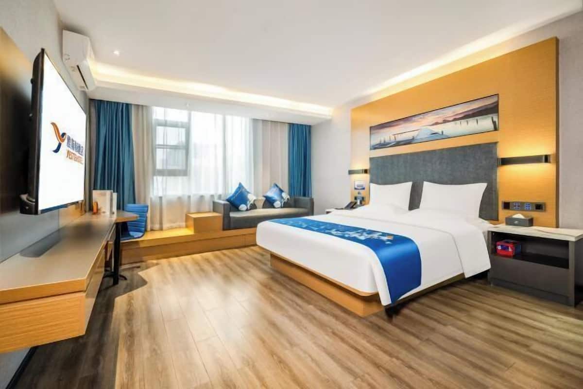 Ein modernes Hotelzimmer mit einem großen Bett, einem Schreibtisch, einem Fernseher und einem Fenster mit Vorhängen.