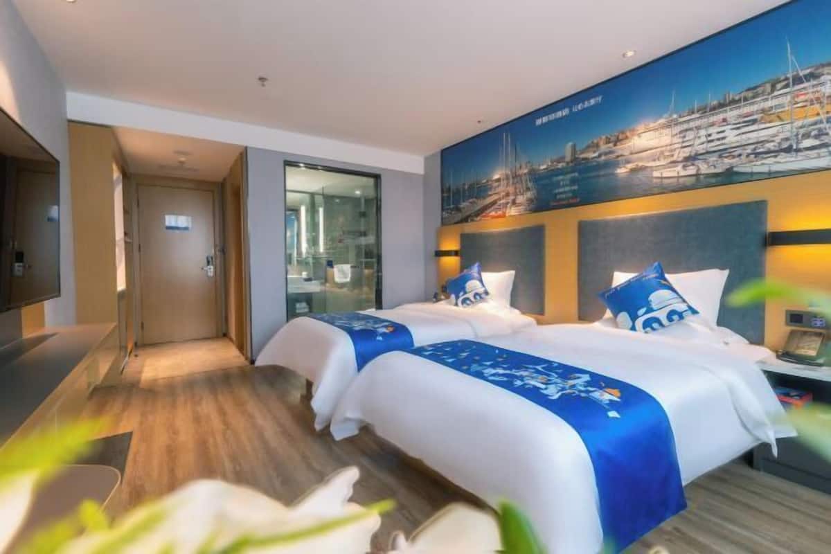 Ein Hotelzimmer mit zwei Betten, einem großen Fenster und Blick auf die Stadt, einem Flachbildfernseher und einem Holzboden.