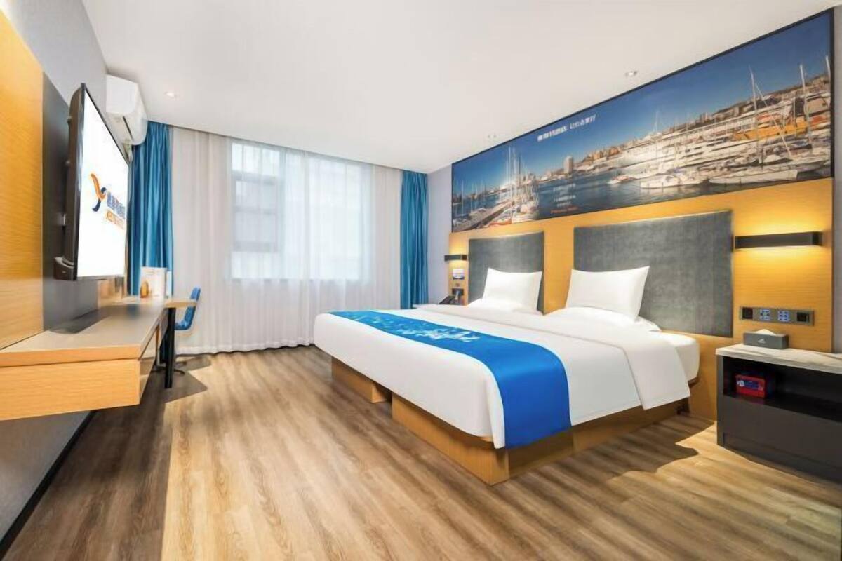 Ein Hotelzimmer mit Bett, Schreibtisch, Fernseher und einem großen Fenster mit Vorhängen.