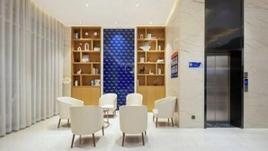 A modern lobby with white chairs, a central blue patterned wall, wooden shelves with various items, and an elevator. - Yeste Hotel (Yulin Jiangbin Road Cross Street) (Yulin)