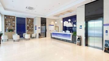 A modern hotel lobby with a reception desk labeled "YESTE," a reception area, seating, and an elevator.