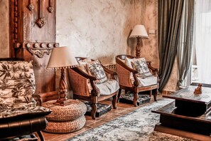 Une pièce avec une cheminée, deux fauteuils, un canapé, une lampe et un tapis à motifs.