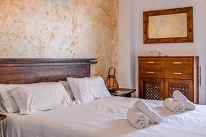Une chambre d’hôtel avec un lit, une tête de lit en bois, du linge de lit blanc, une table de chevet en bois, une commode en bois avec des tiroirs et un miroir mural.