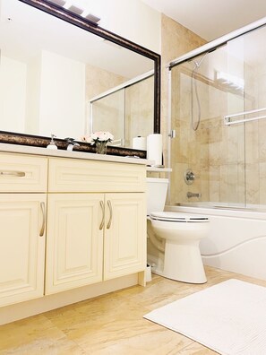 A modern bathroom with a beige vanity, a large mirror, a toilet, and a glass-enclosed shower area.