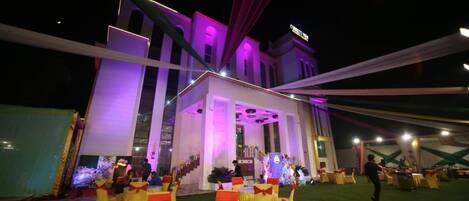 Un espacio al aire libre para eventos con mesas y sillas, una escalera y un edificio con ventanas iluminadas.