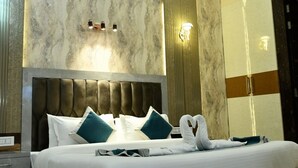 A modern bedroom with a large bed, a ceiling fan, recessed lighting, and a marble-patterned wall. - Corbett View Banquets and Resorts (Moradabad)