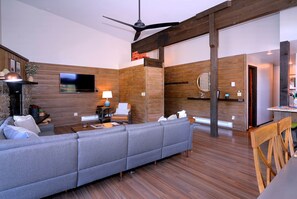A modern living room with a grey sectional sofa, wooden walls, a flat-screen TV, and a ceiling fan. - Dogwood at Outrun - 3 BR, Hot tub, Shuttle (Mt. Crested Butte)