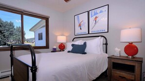 Un dormitorio con cama, dos lámparas de pared, una mesita de noche y dos cuadros enmarcados.