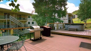 Una terraza con una parrilla, mobiliario exterior y vistas a un edificio de varios pisos.