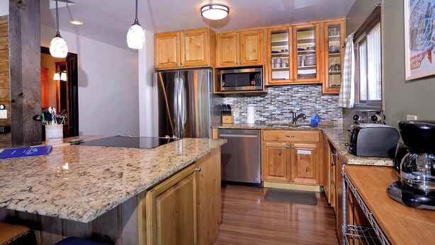 Una cocina moderna con armarios de madera, electrodomésticos de acero inoxidable, encimeras de granito e iluminación colgante.