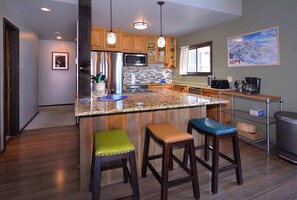 A modern kitchen with a central island, bar stools, wooden cabinets, stainless steel appliances, and a hanging light fixture. - Dogwood at Outrun - 3 BR, Hot tub, Shuttle (Mt. Crested Butte)
