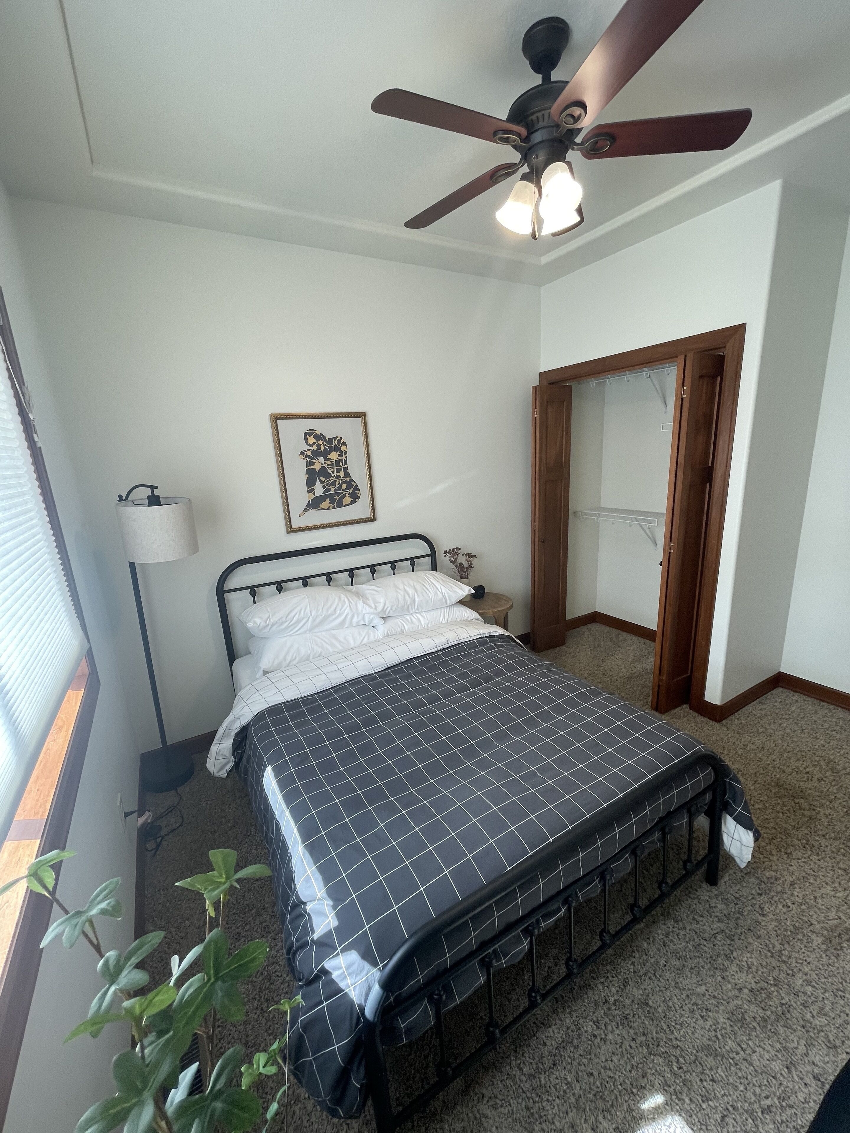 Ein Schlafzimmer mit Bett, Deckenventilator, Nachttischlampe, einem gerahmten Bild und einer Tür.