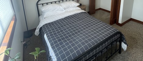 Ein Schlafzimmer mit Bett, Deckenventilator, Nachttischlampe, einem gerahmten Bild und einer Tür.