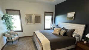 A bedroom with a bed, a ceiling fan, a window, a chair, and a plant. - Friendly Falls Staycation (Sioux Falls)