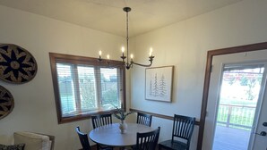 A dining area with a round table, chairs, a chandelier, and a door leading to a balcony. - Friendly Falls Staycation (Sioux Falls)