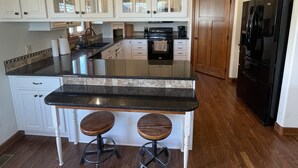A kitchen with white cabinets, a black refrigerator, and two stools. - Friendly Falls Staycation (Sioux Falls)