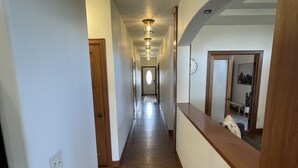 A narrow hallway with wooden flooring, white walls, and a wooden door at the end. - Friendly Falls Staycation (Sioux Falls)