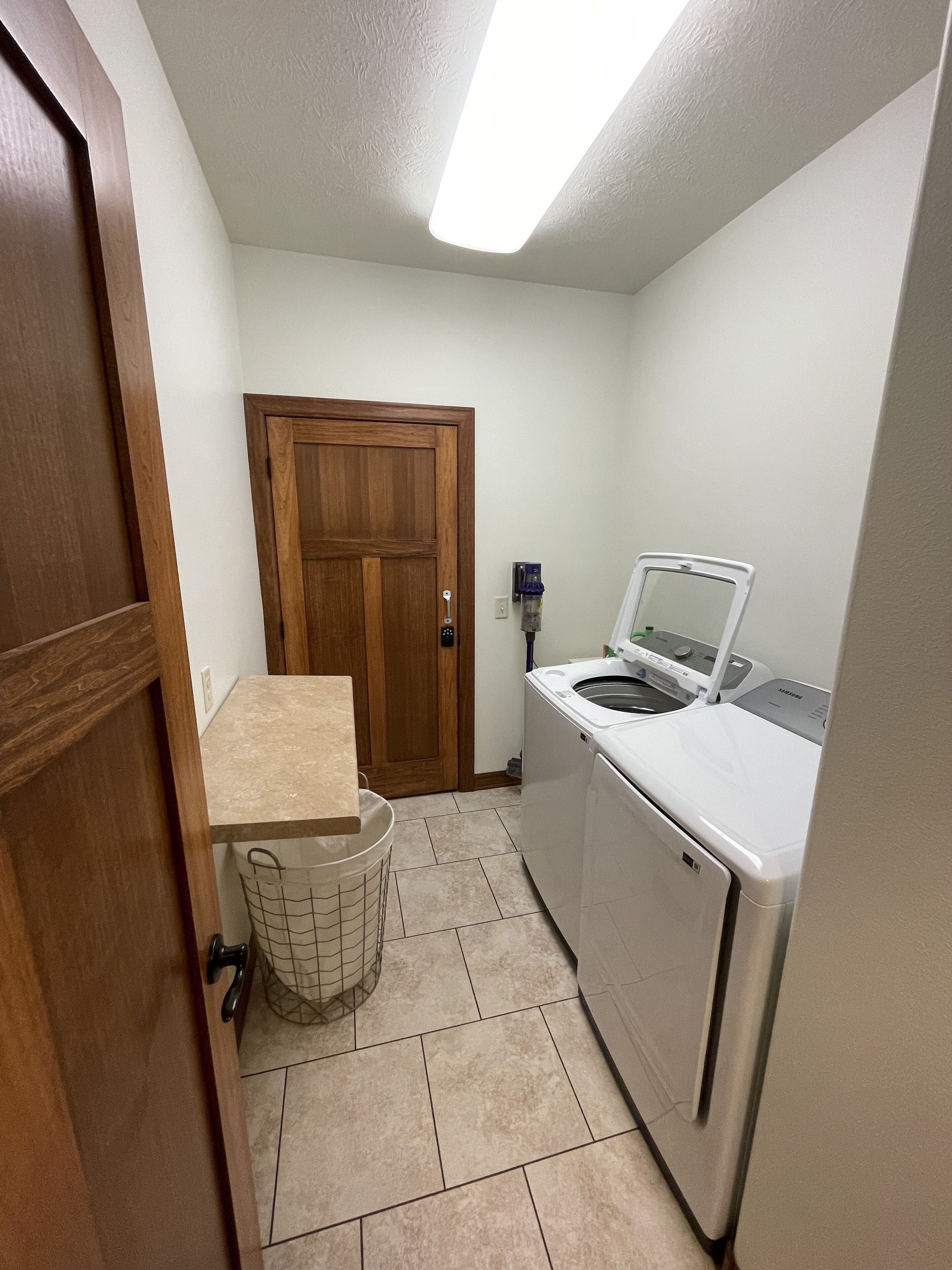 Un cuarto de lavado con lavadora, secadora, una puerta de madera y piso de baldosas.