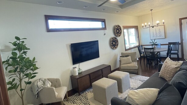 A living room with a flat-screen TV, a ceiling fan, a dining area with a table and chairs, and a potted plant. - Friendly Falls Staycation (Sioux Falls)