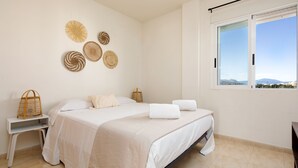 Ein Schlafzimmer mit Bett, weißen Wänden und einem Fenster mit Blick.
