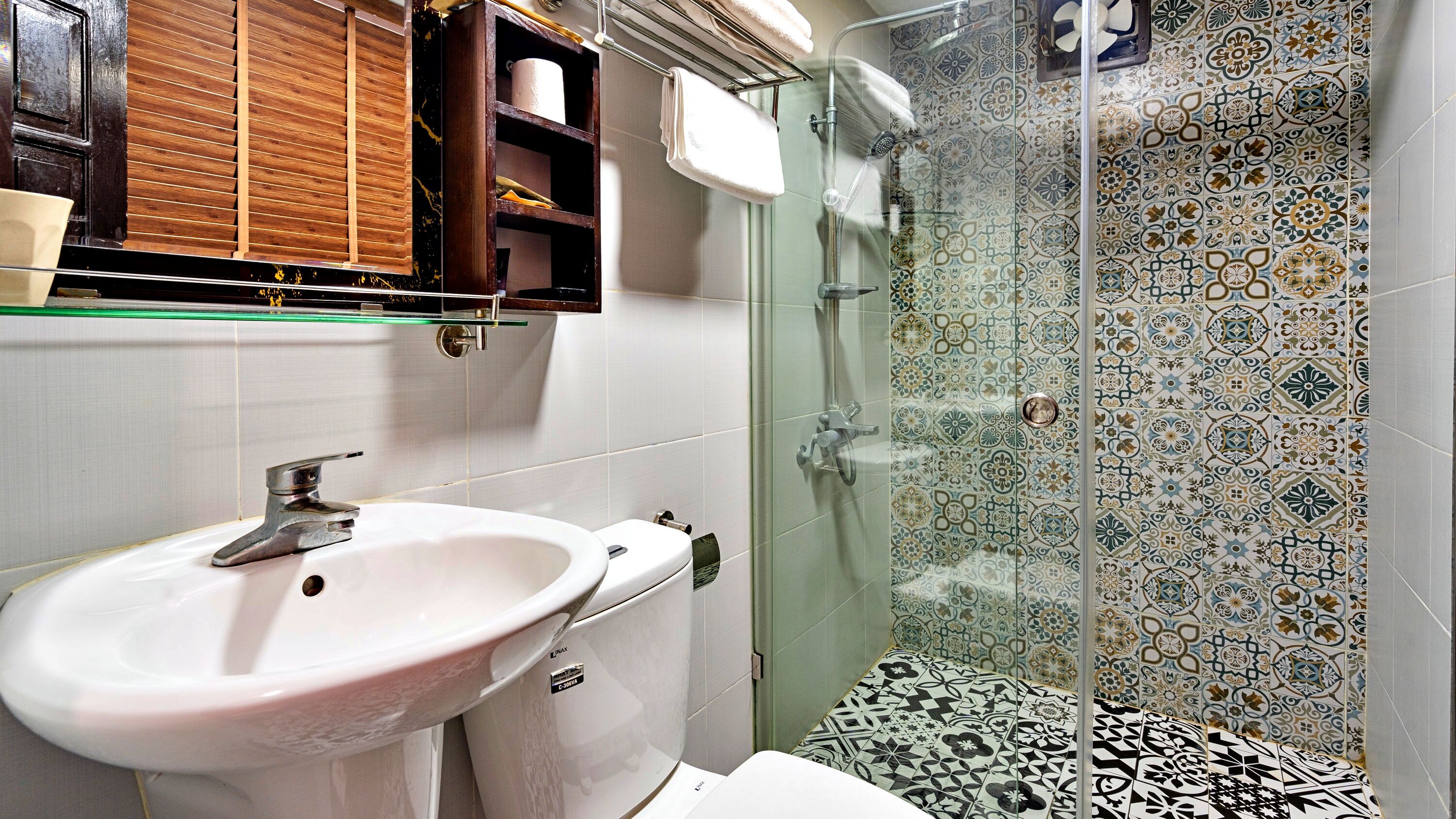 A bathroom with a white sink, a glass shower enclosure, and patterned tiles.