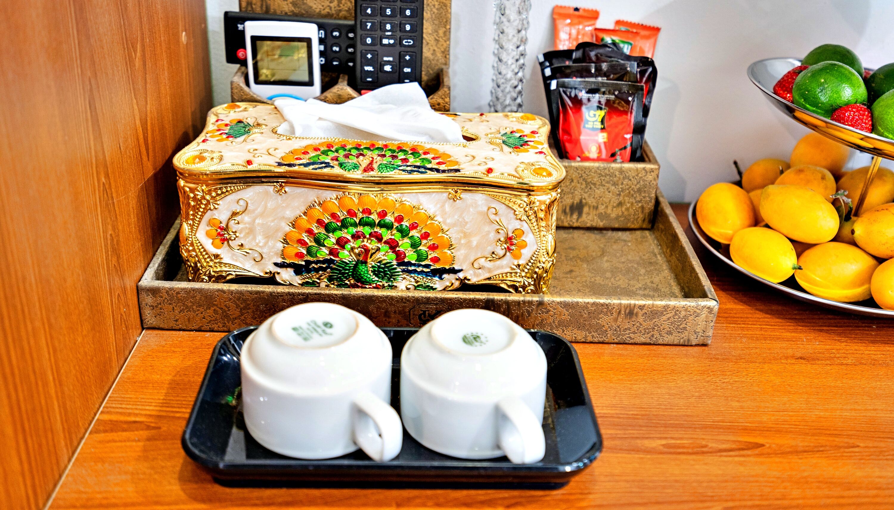A decorative box with a tissue, two white cups, and a tray with lemons.