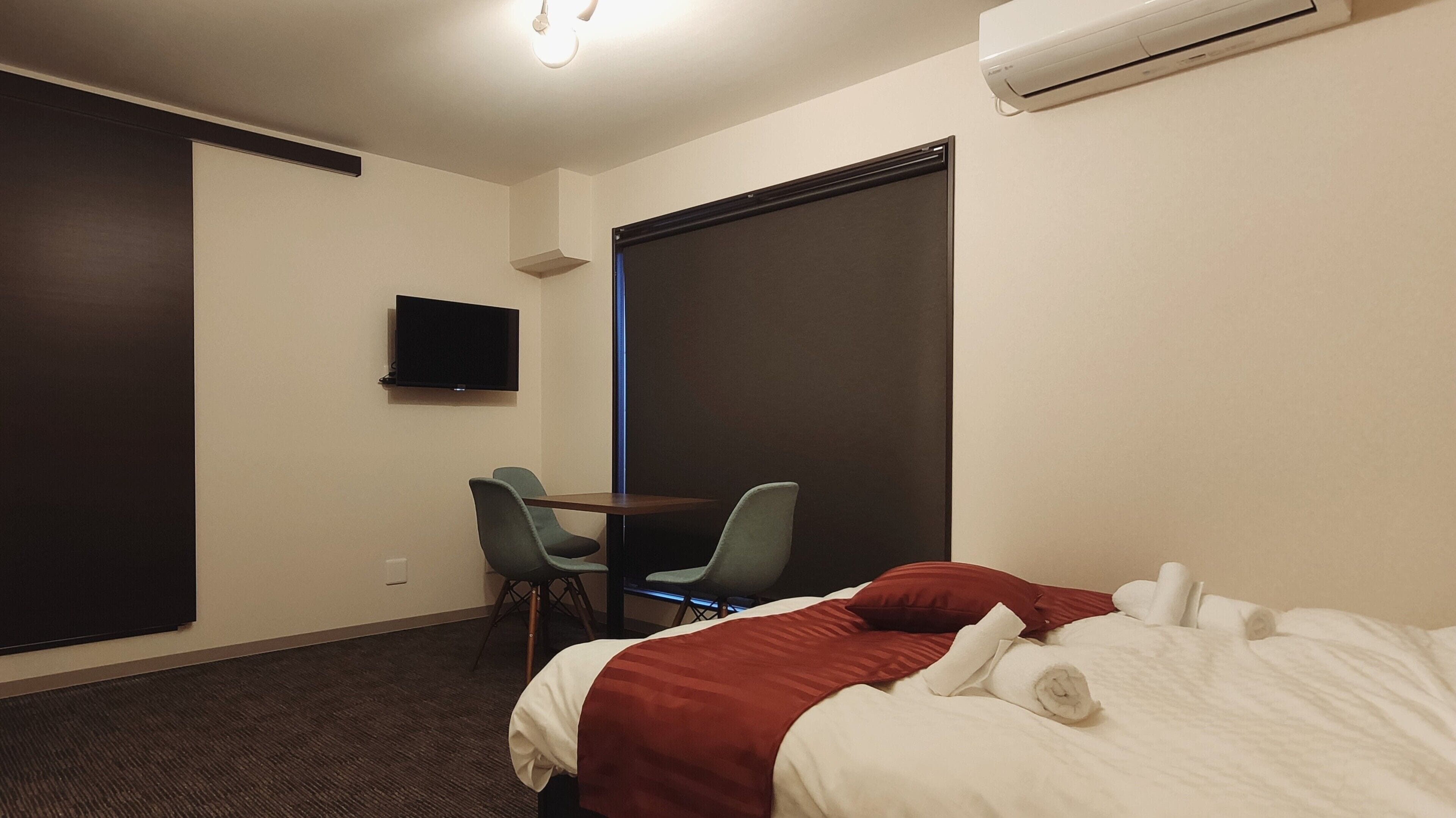 A hotel room with a bed, a desk, a chair, a television, and an air conditioning unit.
