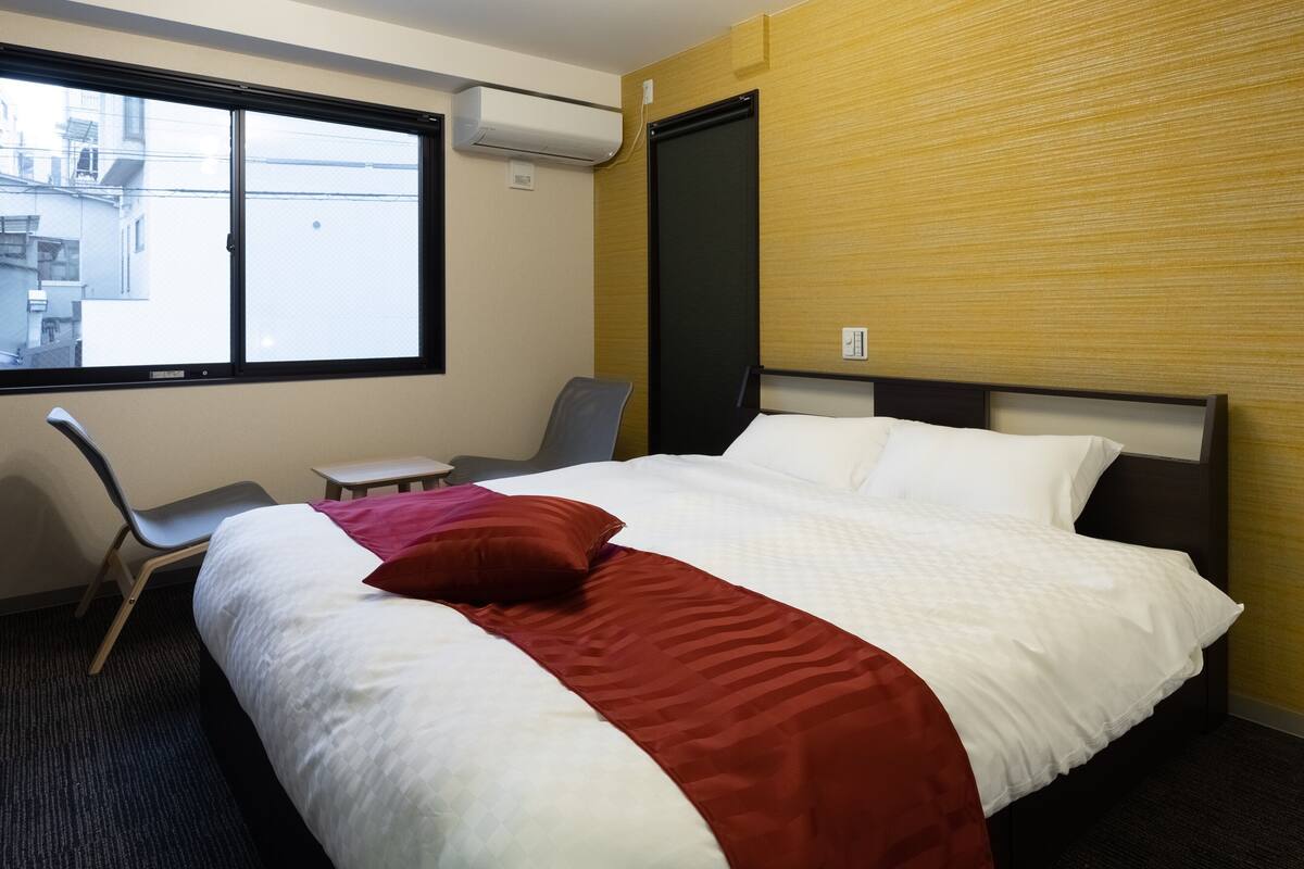 A hotel room with a bed, a desk, a chair, and a window.