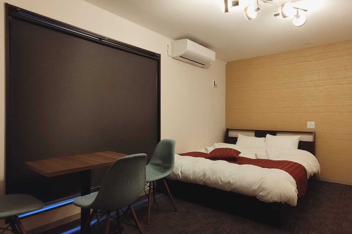 A hotel room with a bed, a desk, a chair, and an air conditioning unit.