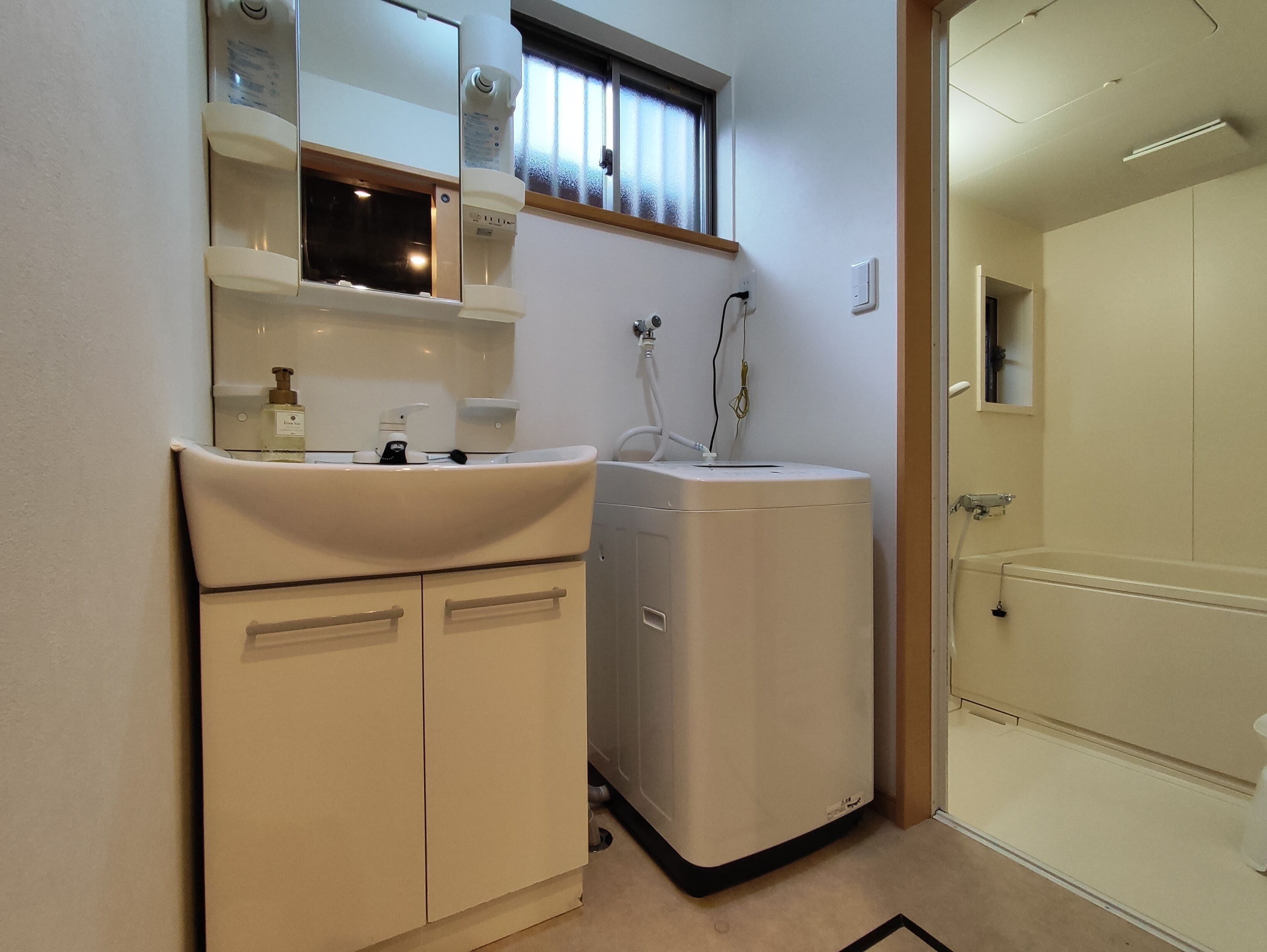 A compact bathroom with a sink, mirror, and a compact washing machine.