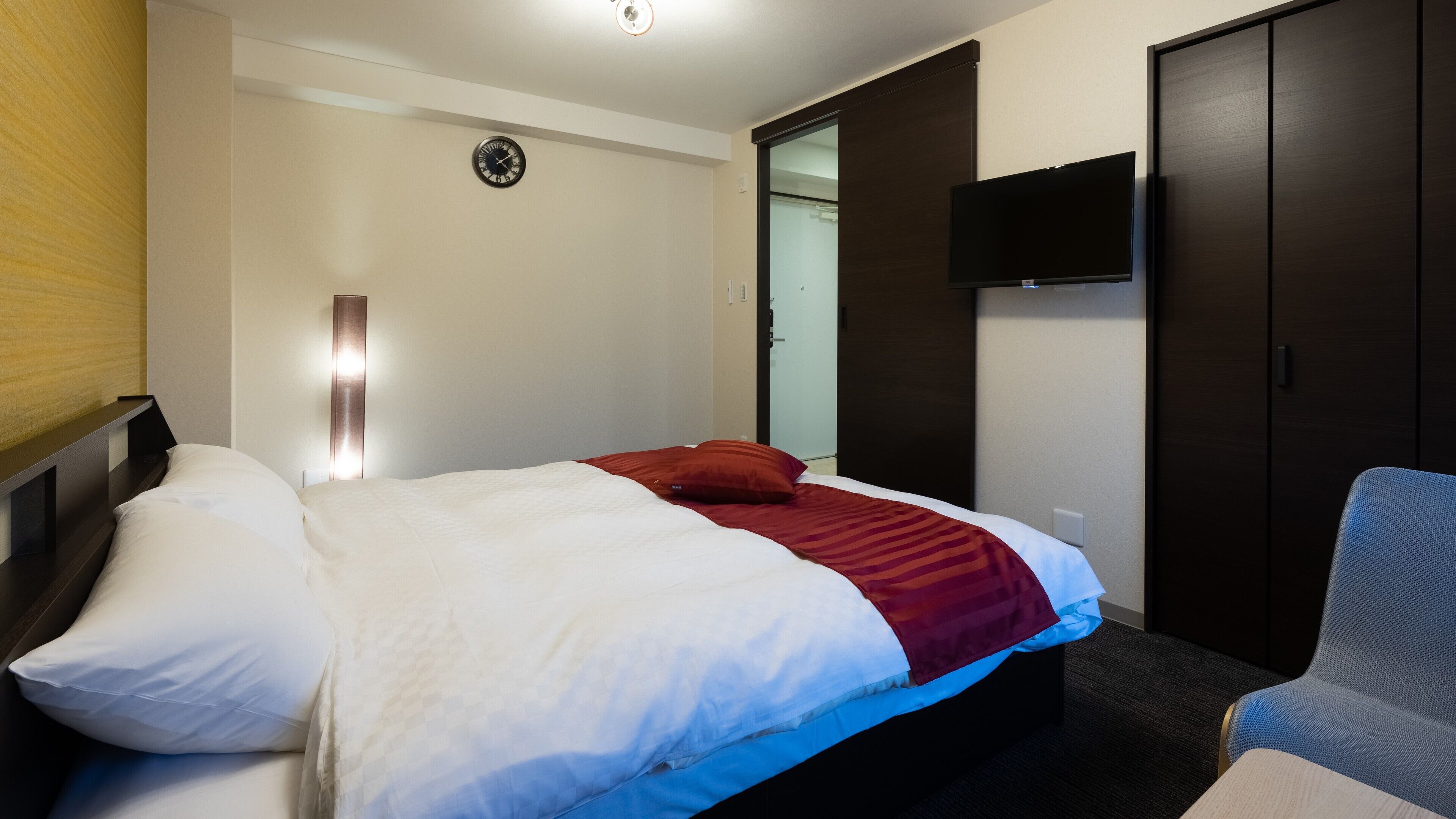 Ein Hotelzimmer mit einem Bett, einem an der Wand montierten Fernseher und einem Kleiderschrank.