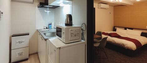 Una habitación de hotel compacta con kitchenette, una cama con una manta roja y una pequeña zona de estar.