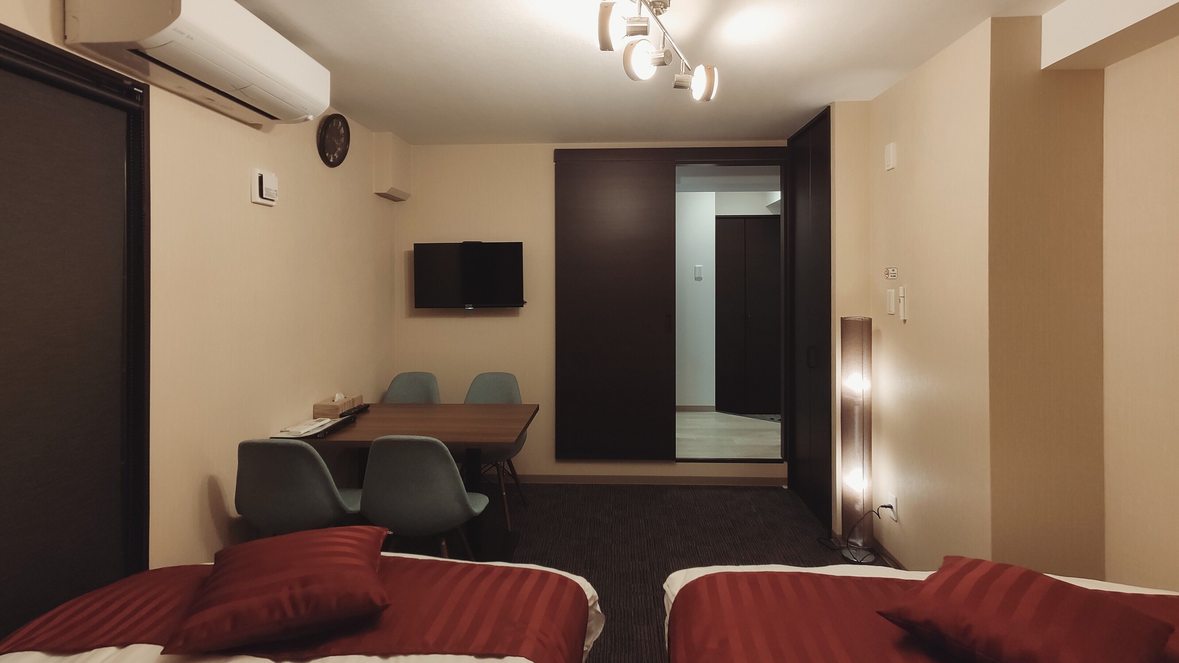 A hotel room with two beds, a desk with chairs, a TV, and a door leading to a balcony.