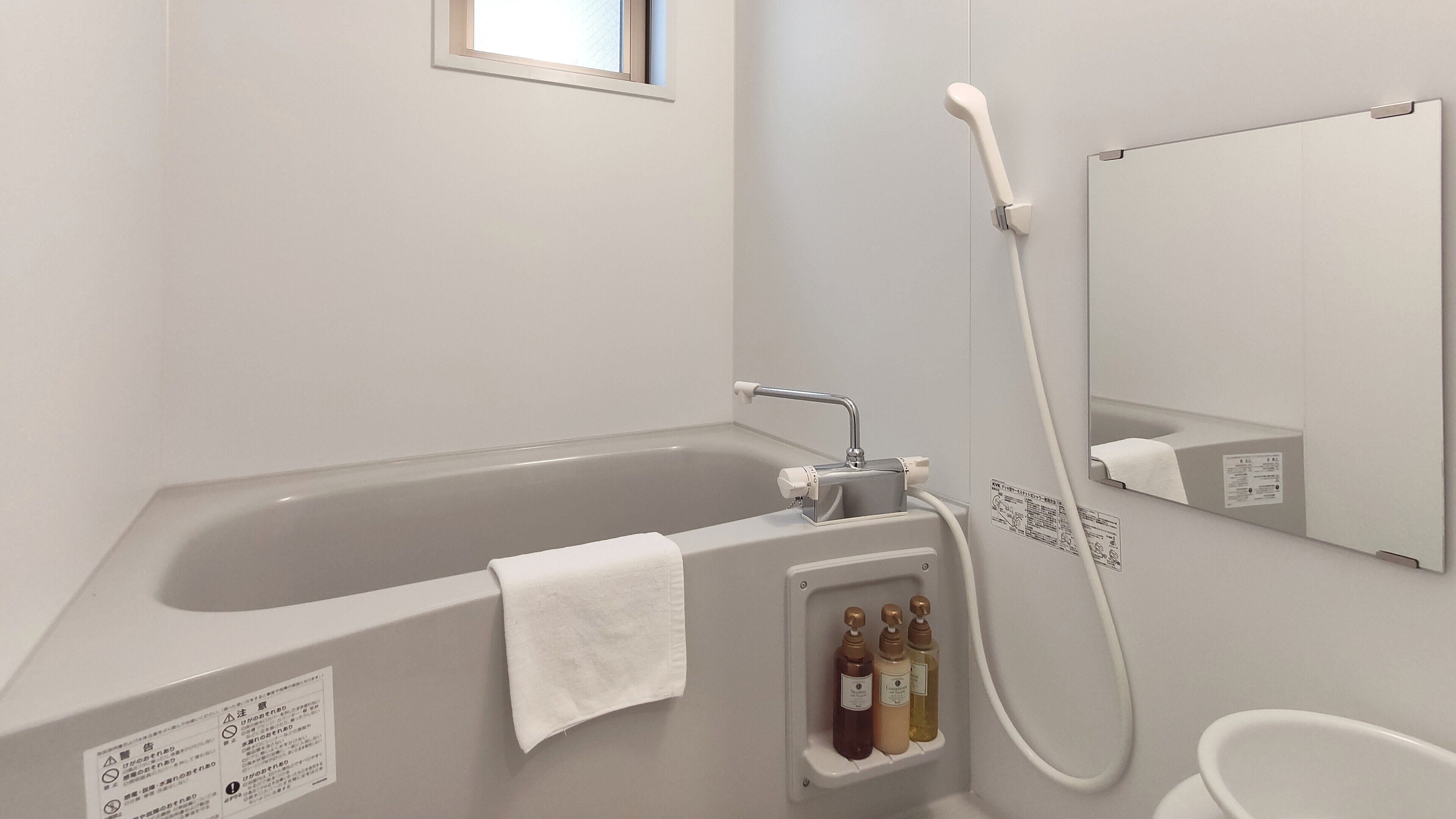 A bathroom with a bathtub, a handheld showerhead, and a built-in shelf with toiletries.