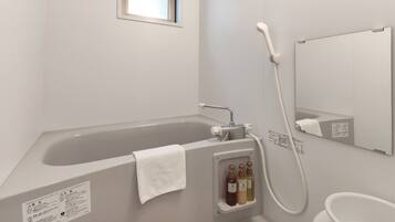 A bathroom with a bathtub, a handheld showerhead, and a built-in shelf with toiletries.