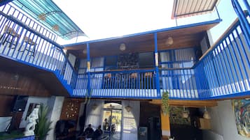 A modern hotel atrium with a central open space, multiple balconies with blue railings, and a seating area with sofas and a small table.