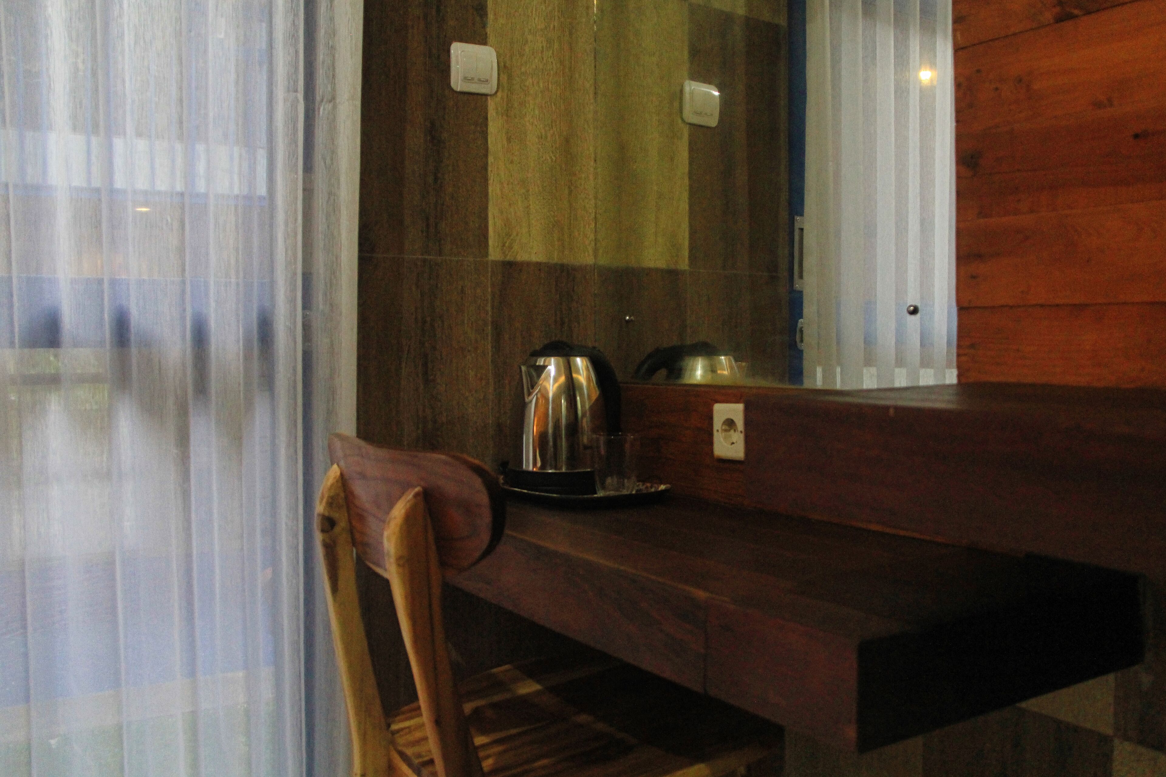 A wooden counter with a kettle and a cup, a chair, and a mirror reflecting the room.