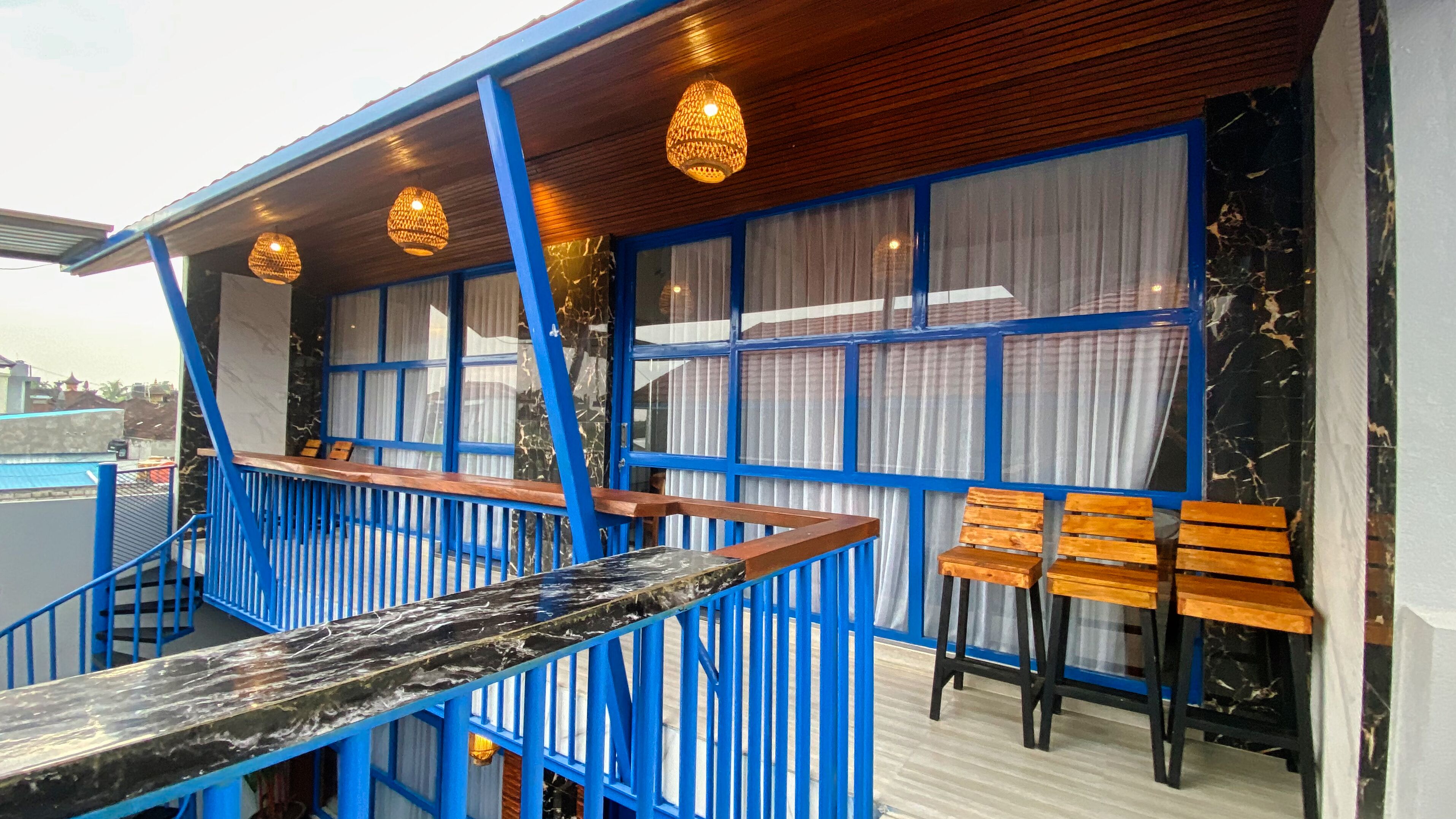 A bar area with blue railings, wooden chairs, and hanging pendant lights.
