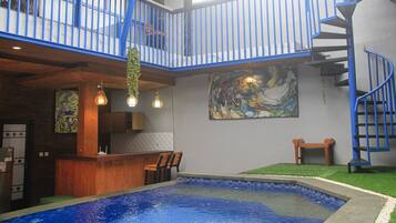 A pool area with a wooden bar and seating, a staircase, and a large abstract painting on the wall.