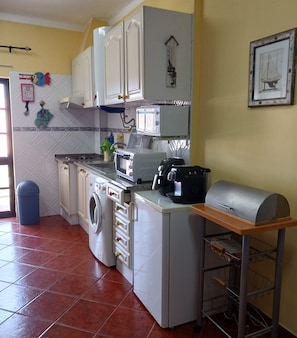 Une cuisine compacte avec des meubles blancs, un lave-linge, un four à micro-ondes et un gril.