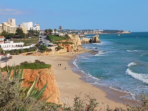 A coastal landscape with a beach, rocky cliffs, and a cityscape in the background. - Villa Vau (Praia Do Vau)
