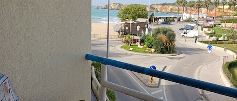 A balcony with a view of a beach, a chair, and a railing.