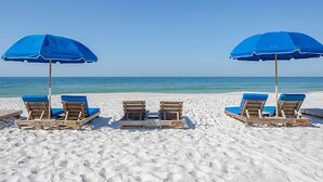 A beach with two rows of wooden lounge chairs under blue umbrellas, facing the ocean.