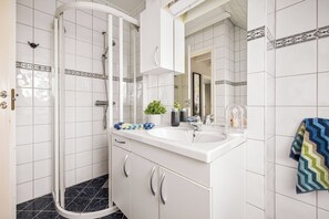 Un baño moderno con cabina de ducha de vidrio, un lavabo blanco con un espejo encima y un perchero con una toalla estampada.
