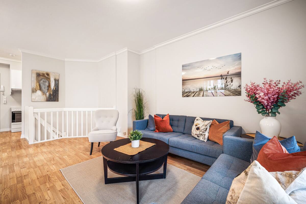 A modern living room with a blue sofa, a white chair, a coffee table, and a painting of a sunset over water.