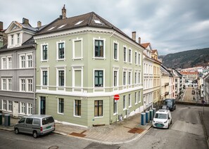 Vista de la calle que muestra una hilera de edificios históricos, un camino estrecho, coches estacionados y un cielo despejado.