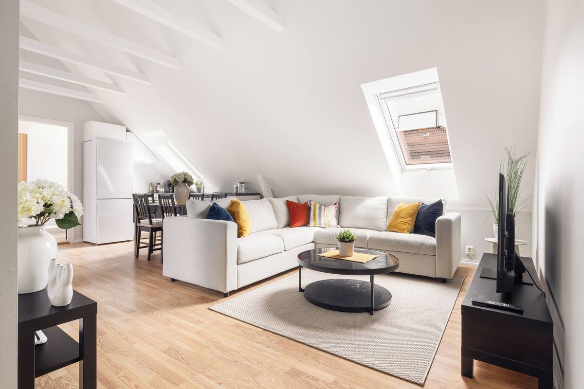A modern living room with a white sofa, a round coffee table, and a dining area with a white refrigerator.