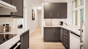 A modern kitchen with dark cabinets, a white countertop, and a built-in dishwasher. - Rosen Apartment  (Bergen)
