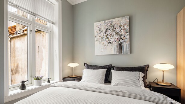 A bedroom with a large bed, two bedside tables with lamps, a window with blinds, and a wall-mounted painting. - Rosen Apartment  (Bergen)