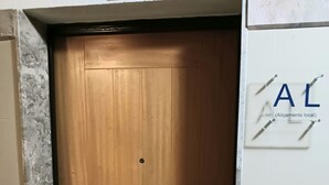 Een houten deur met een metalen handvat, een bord met de letters 'AL' en de tekst 'Alojamento local' aan de rechterkant van de muur.